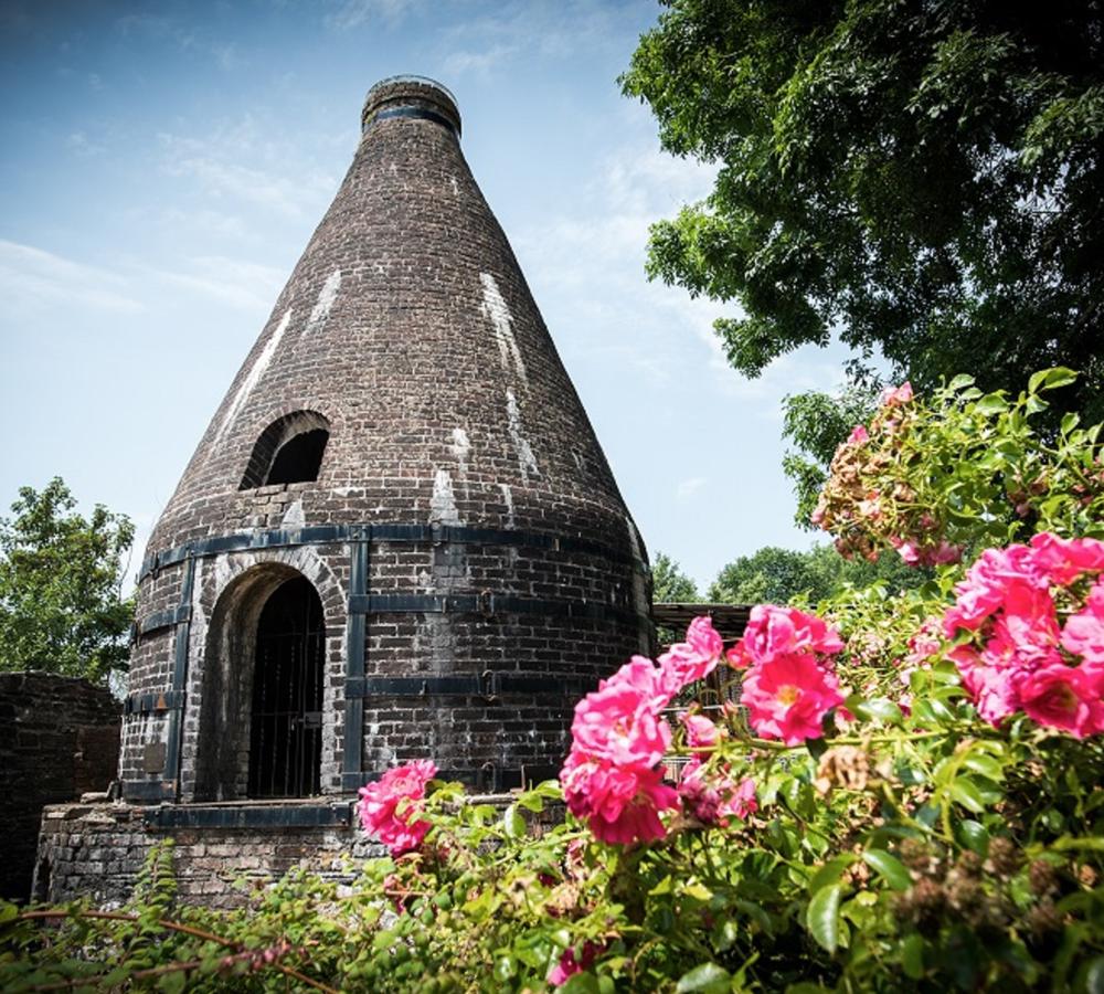 The original conical pottery kiln at Nantgarw China Works Museum, surrounded by flowers and trees.